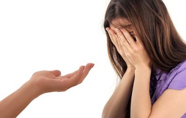 Woman sits with head in hands as her therapist reaches out a helping hand at counselling.